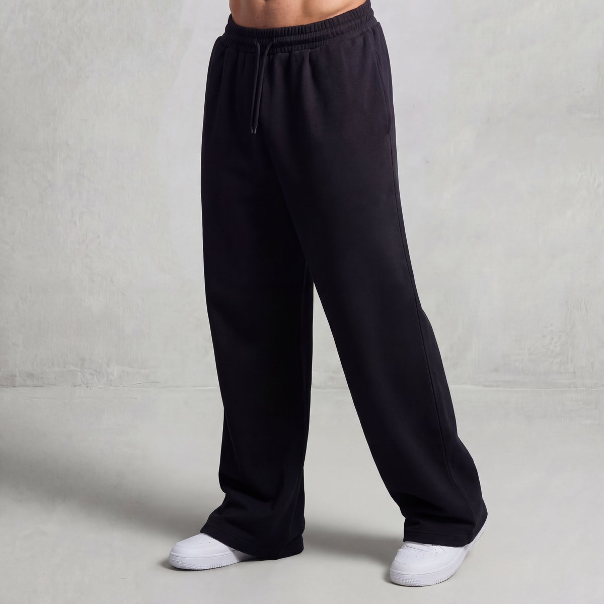 GMAN Essentials Loose Sweatpants in Black, oversized wide-leg fit, worn with white sneakers on a person.